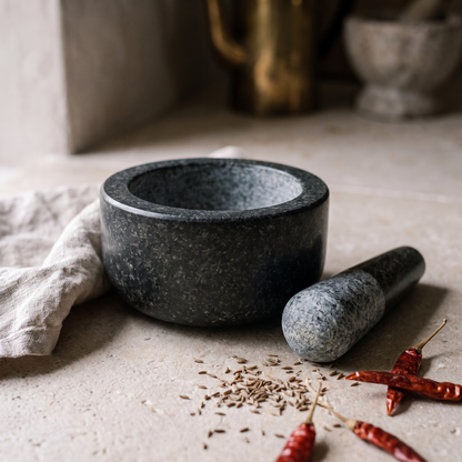 The mortar and pestle on a kitchen worktop with cumin seed and dried chillies