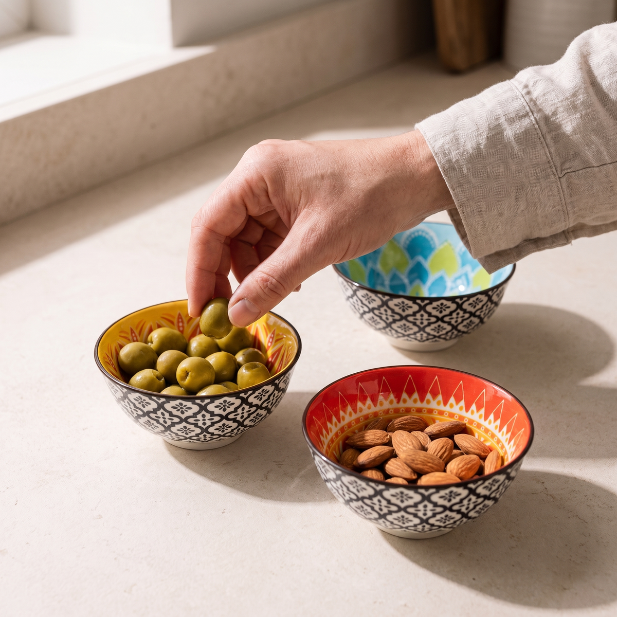 The bowls in use holding olives and almonds, with a hand reaching in