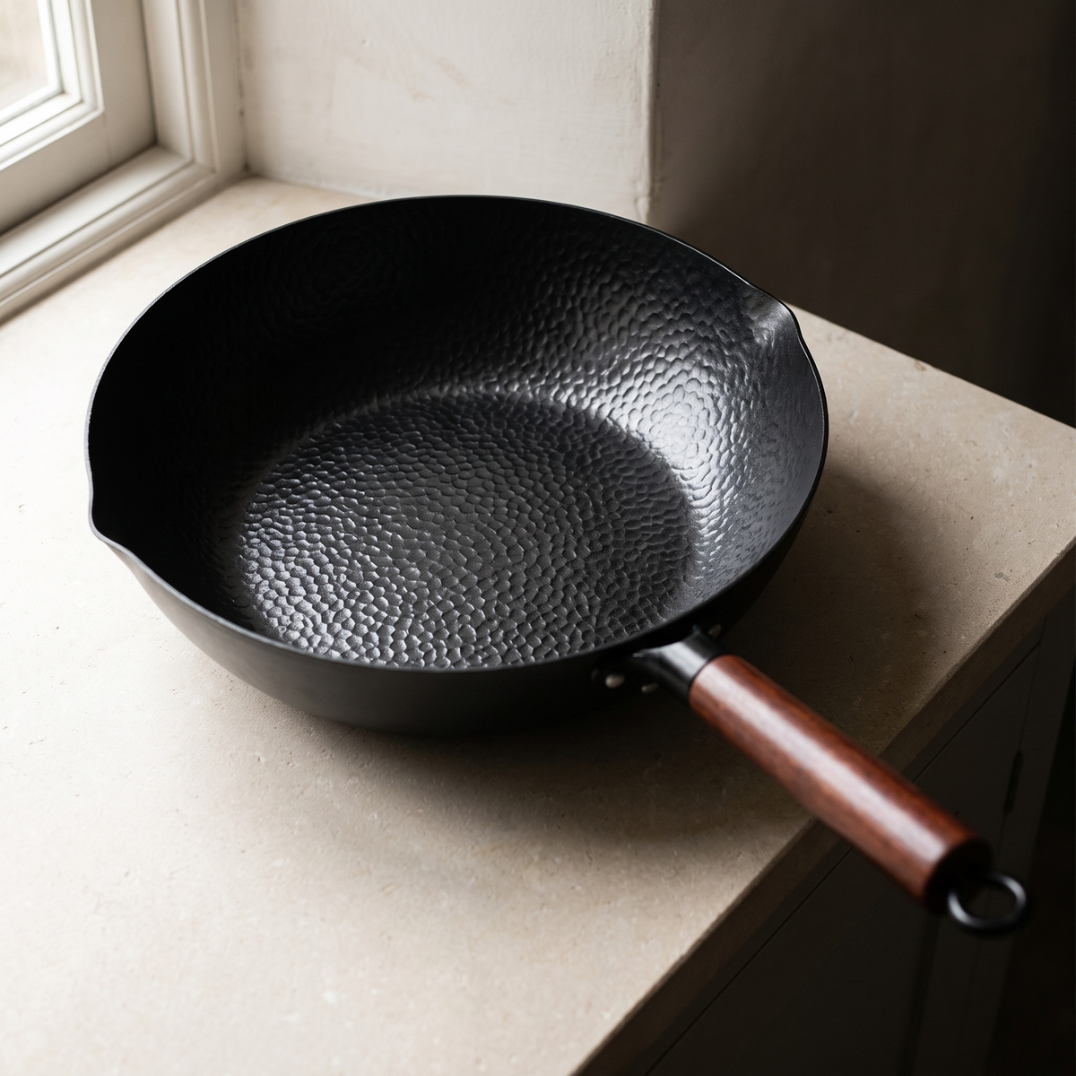Hammered iron wok seen from above on a limestone worktop