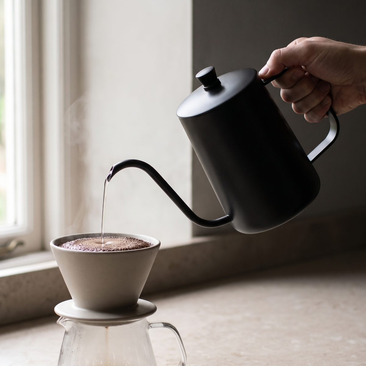 Pouring a thin steady stream into a ceramic dripper over a glass carafe