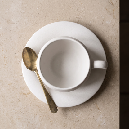 Seen from above, the saucer holding the cup and a brass teaspoon